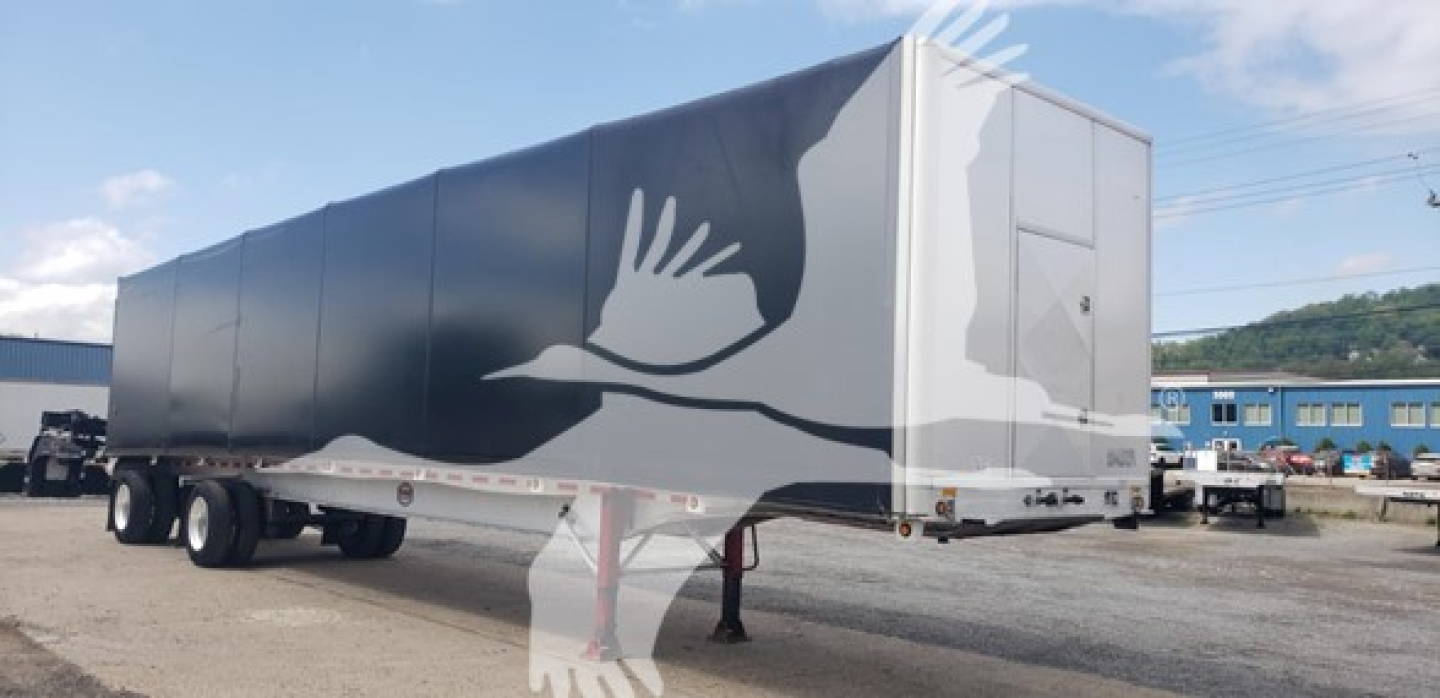 Mac Alum flatbed trailer showing curtain-side design and logo on gray panels.