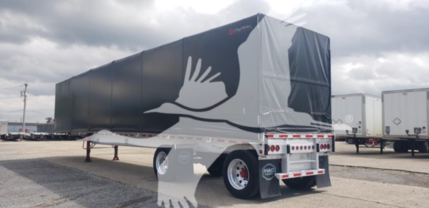 Flatbed trailer with black curtainside and white graphic bird logo, Mac aluminum trailer, rear view showing tandem axles and landing gear, stock number 7687.