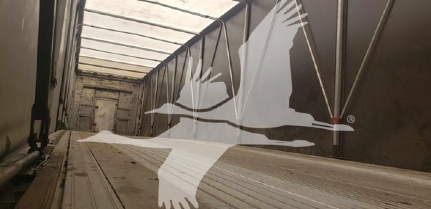 Flatbed trailer interior with corrugated aluminum, door track, and flooring; a large white graphic of a flying bird overlaying the image.