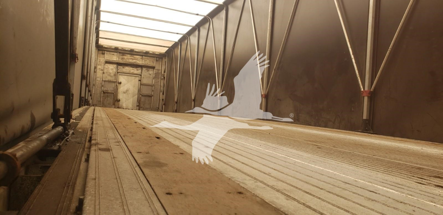 Trailer interior showing empty aluminum cargo floor with rails and wheel wells along the sides.