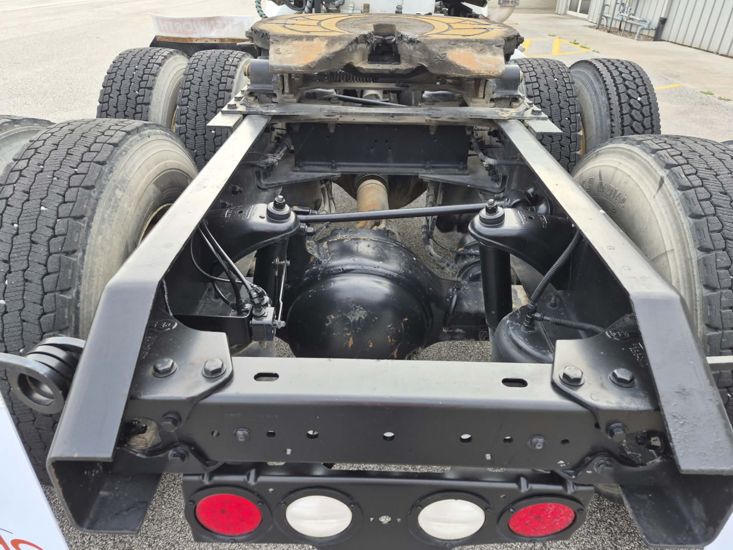 Kenworth T880 chassis view showing rear frame, suspension, axle housings, and drivetrain area with six wheels visible; no cab mounted.