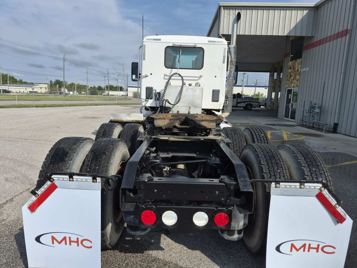 Kenworth T880 conventional daycab chassis rear view showing dual rear axles and fifth wheel mount with MHC logos on white mud flaps.