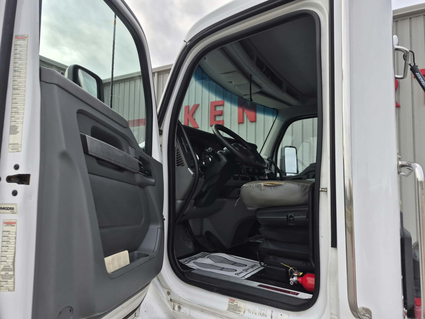 Kenworth T880 cab interior view from open driver door showing steering wheel and driver's seat with dash panel