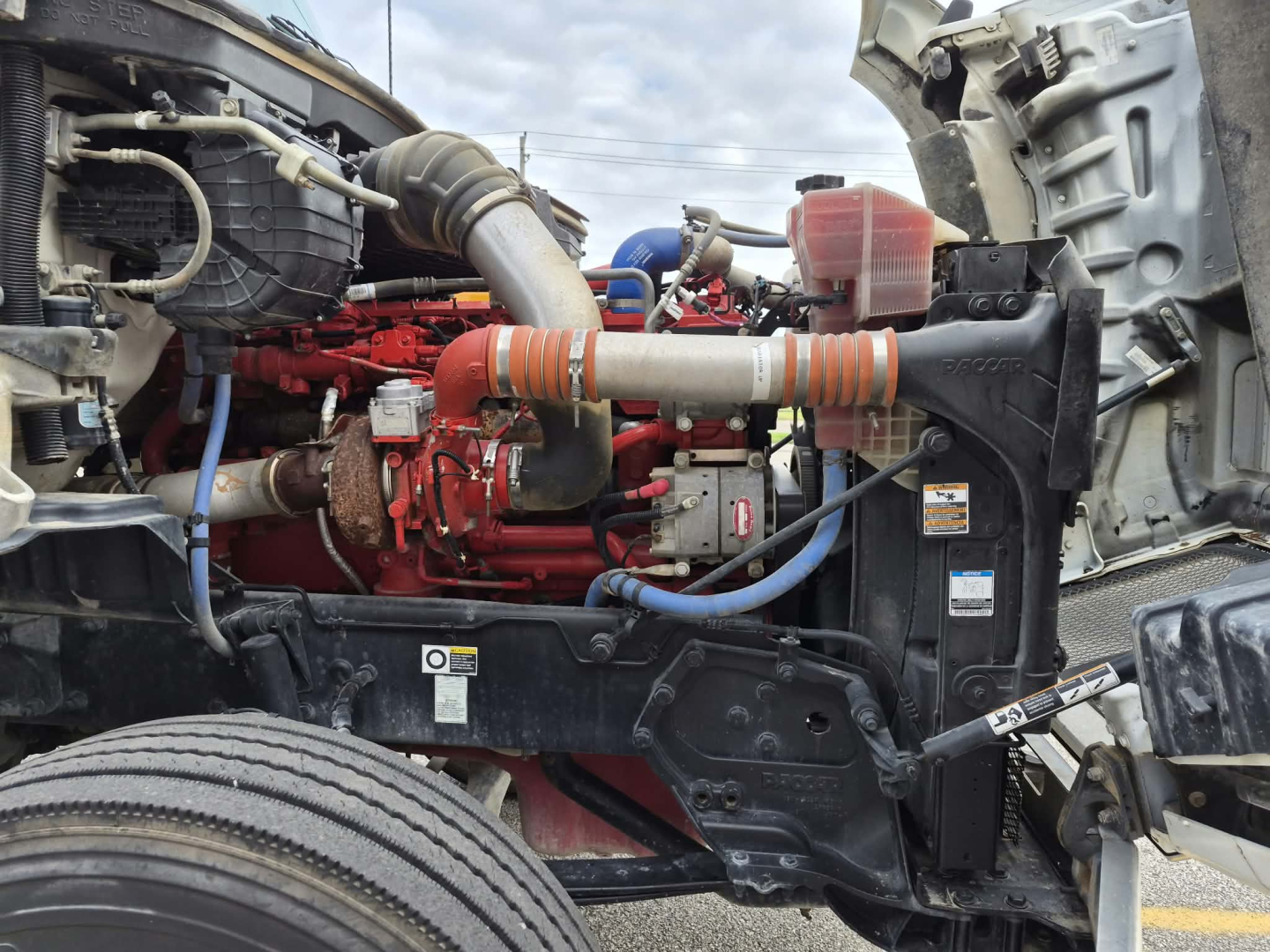 Kenworth T880 engine bay showing red diesel engine, air intake, hoses, radiator, and chassis framing.