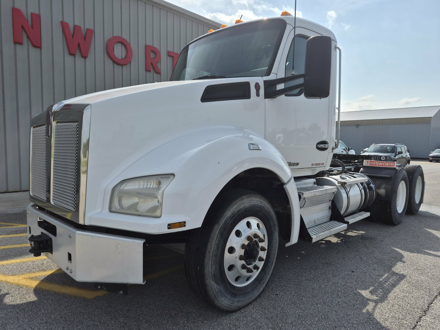 White Kenworth T880 daytime cab tractor front-left view with steps and fuel tanks visible, side mirrors, large grille, and wheel with dual rear axles.