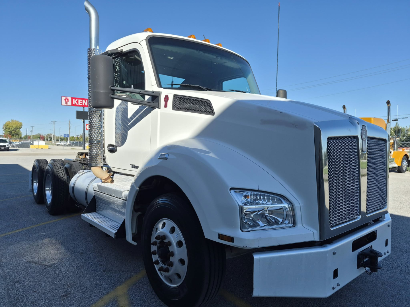 2018 Kenworth T880 conventional daycab truck front and side view showing large grille, chrome bumper, dual fuel tanks, and tall exhaust stack.