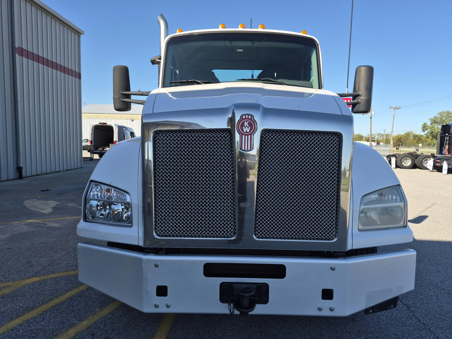 Kenworth T880 front view with chrome grille and large bumper; windshield, side mirrors, and marker lights visible.