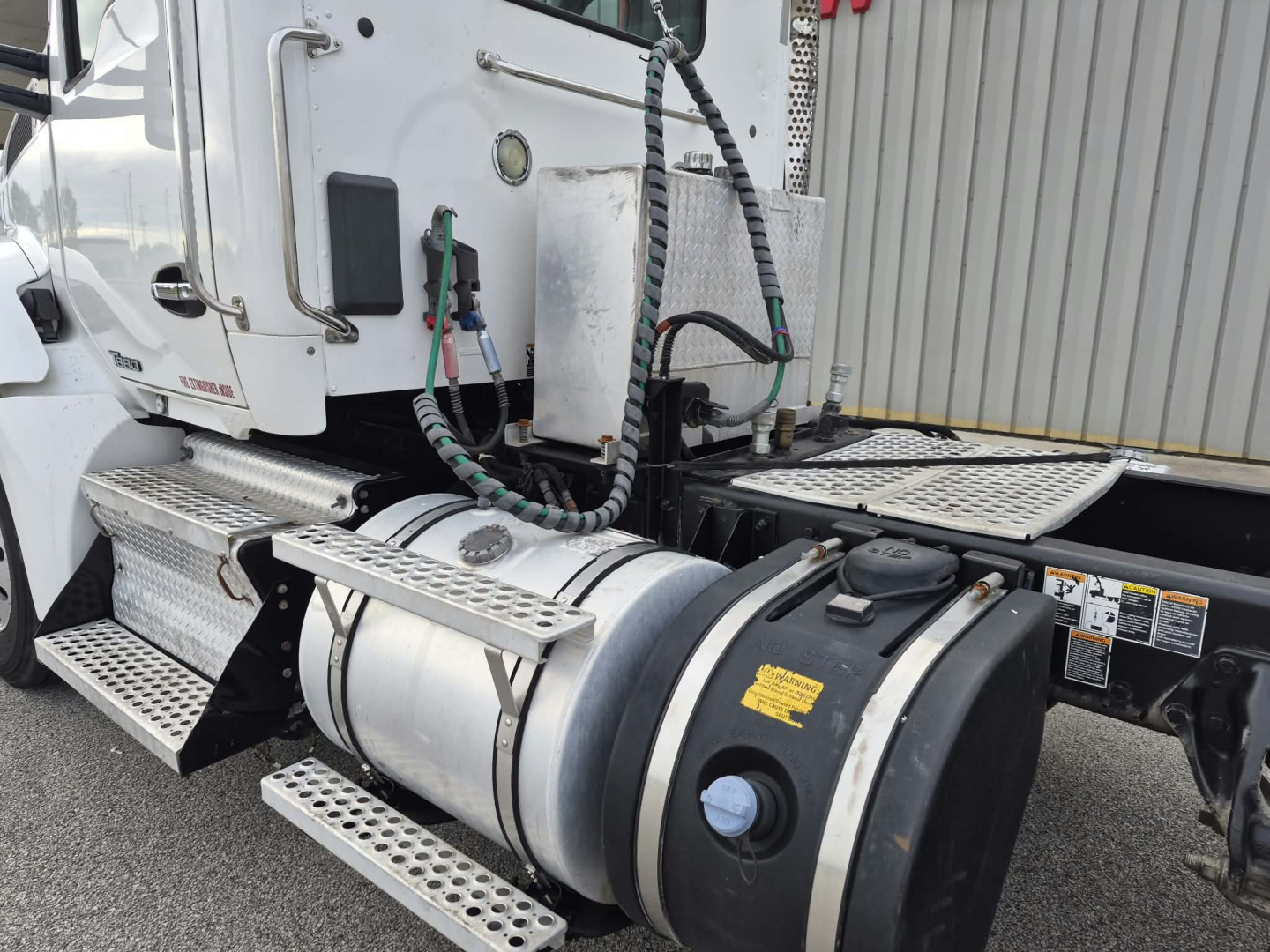 Kenworth T880 truck fuel tank and side view showing polished cylindrical fuel or air reservoir with black cap, steps, mounting, and cab area.