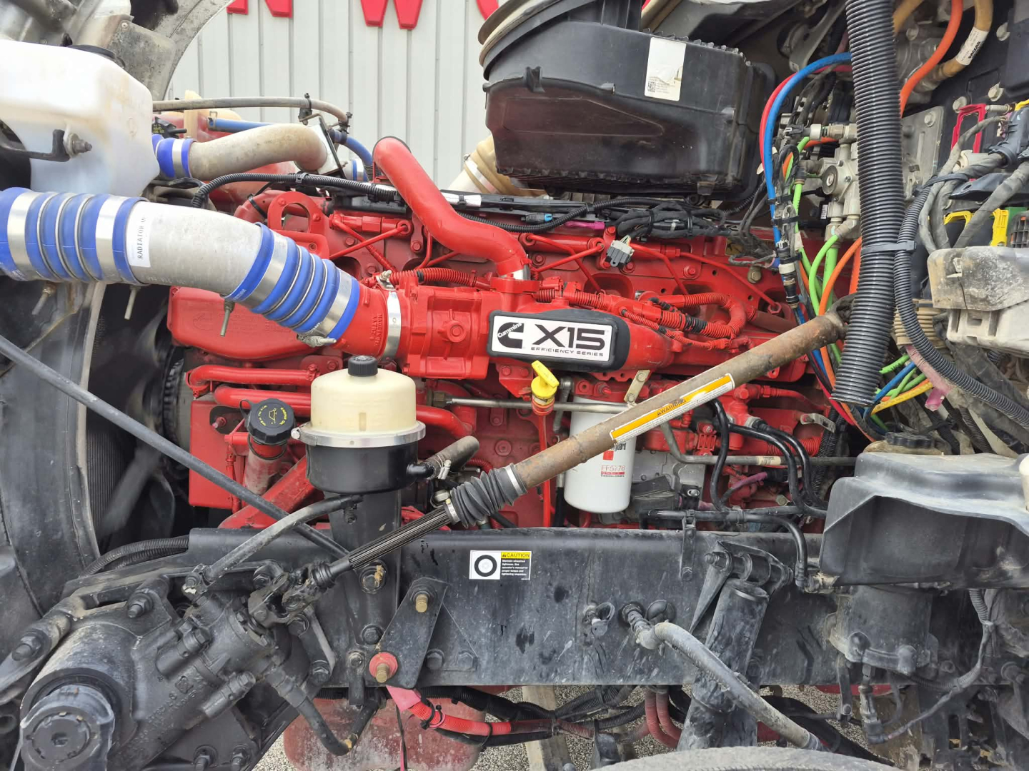 Kenworth T880 engine bay showing red engine with X15 badge and surrounding hoses and wiring.