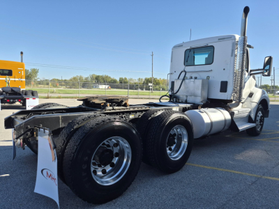 Kenworth T880 conventional daycab tractor with dual rear axles and chrome exhaust stack, white cab, parked in lot.
