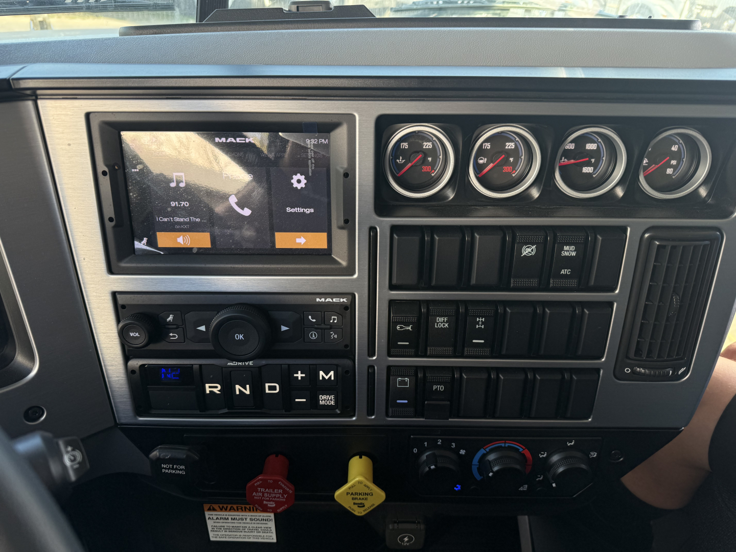 Dashboard of a 2026 Mack PI64 dump truck showing touchscreen infotainment with settings, multiple analog gauges, gear selector, and control switches.