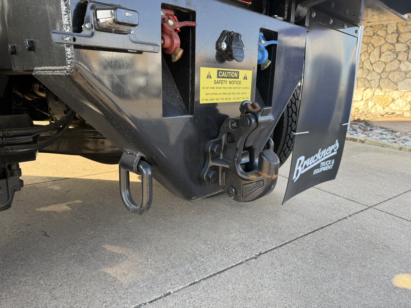 Mack PI64 dump truck rear hitch and bumper with safety sticker and Braden brake component visible.