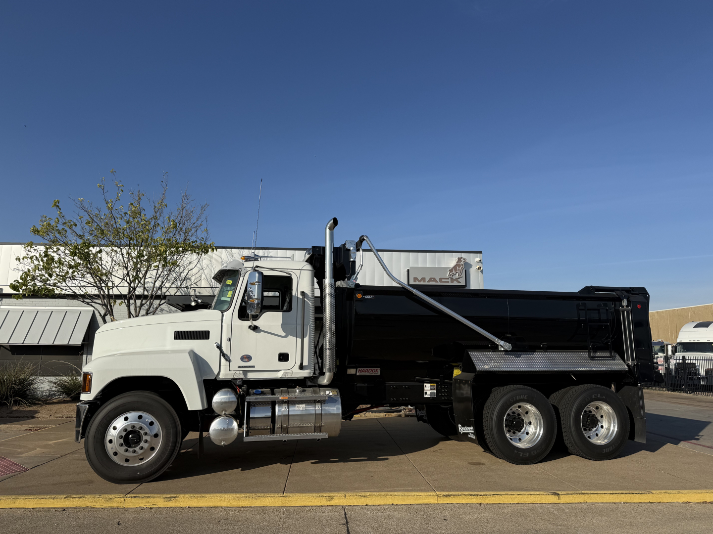 Dump truck side view showing 6-wheel Mack PI64 with black dump bed and chrome fuel tanks.