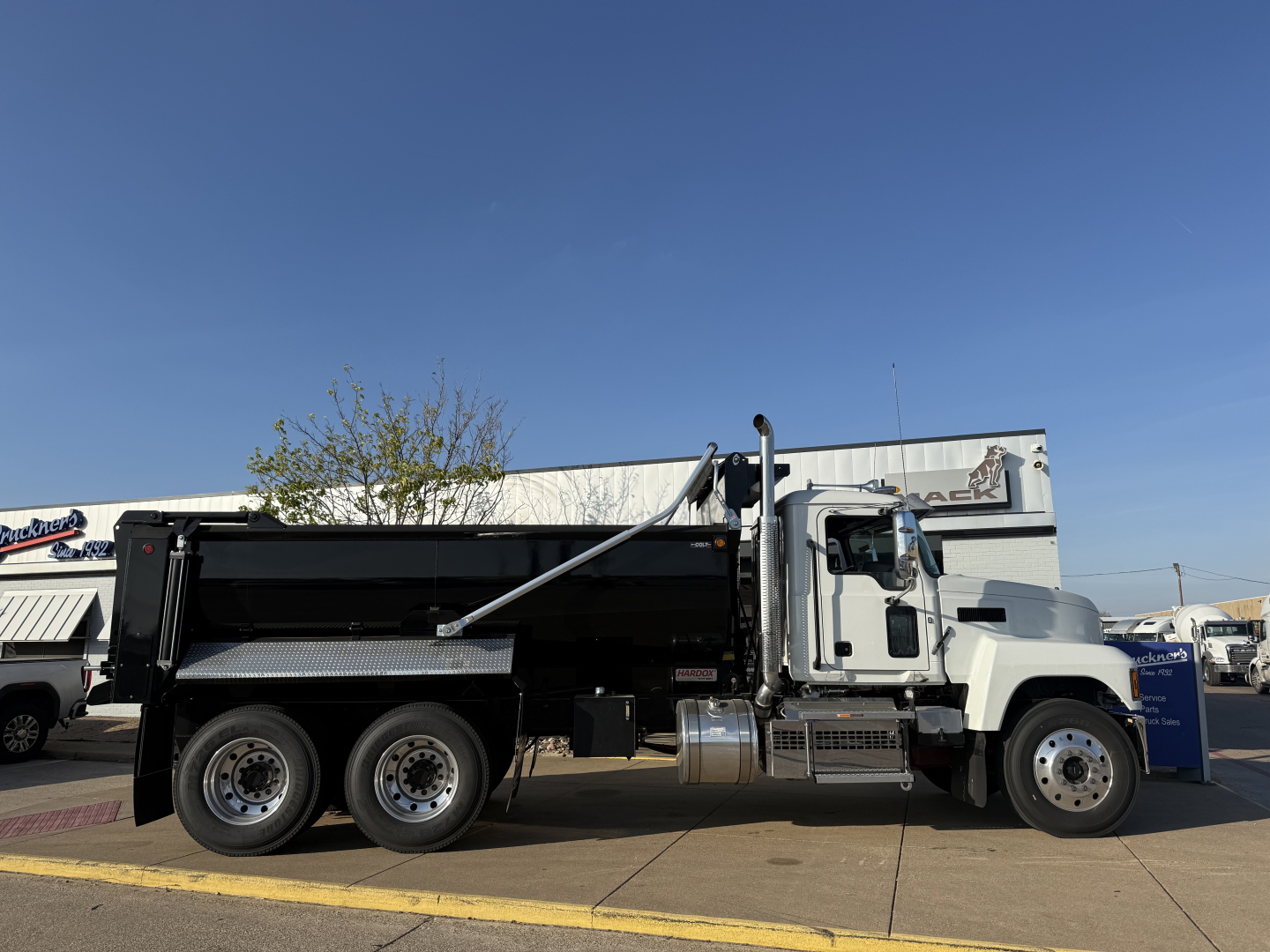 Dump truck side view showing Mack PI64 dump body and chrome fuel tanks with black dump bed and wheels.