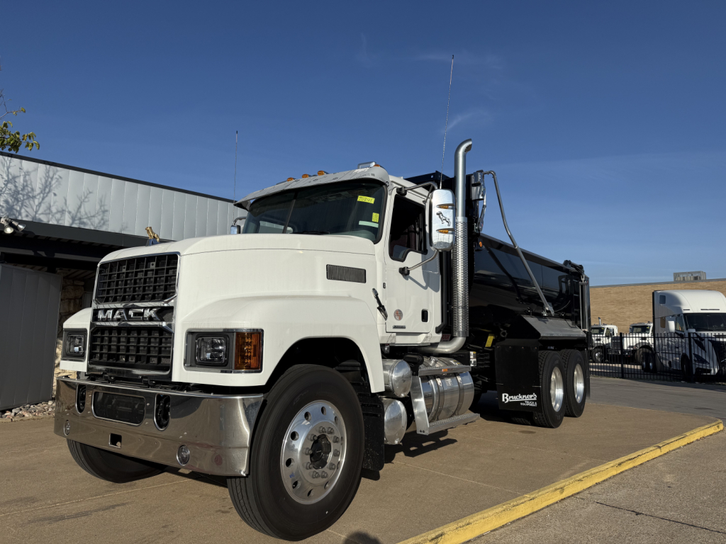 Mack PI64 dump truck in service bay showing front grille with Mack emblem and dual rear axles.