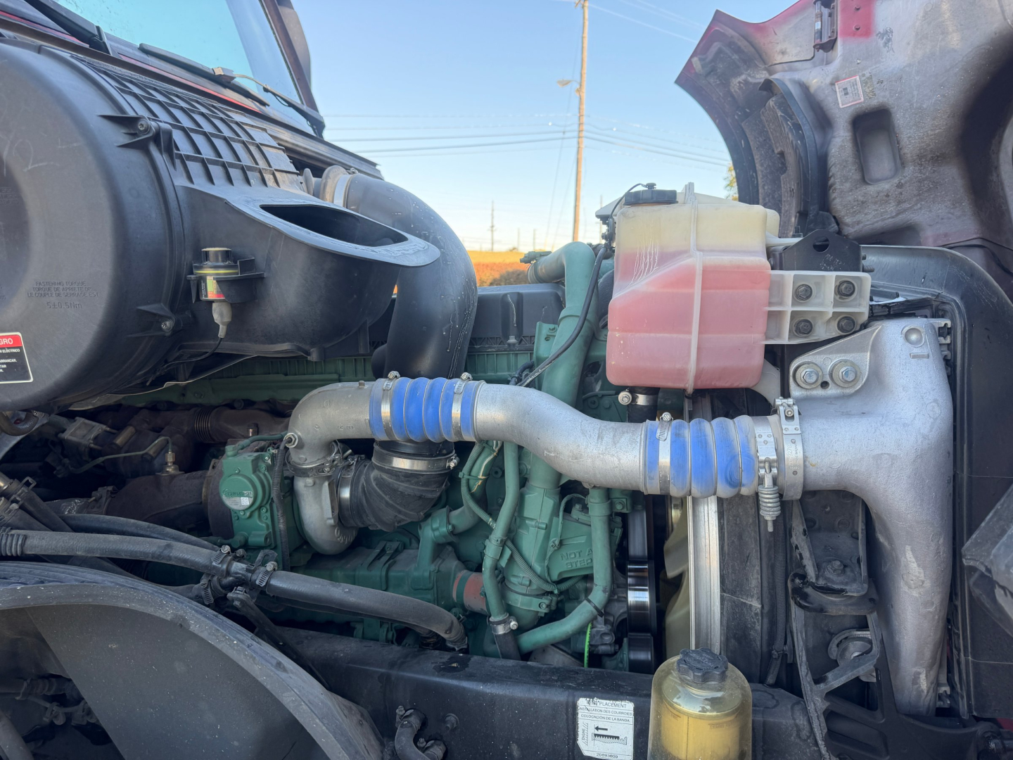 Volvo VNL64T760 engine bay showing coolant reservoir and turbo piping with blue silicone hoses and engine block components.