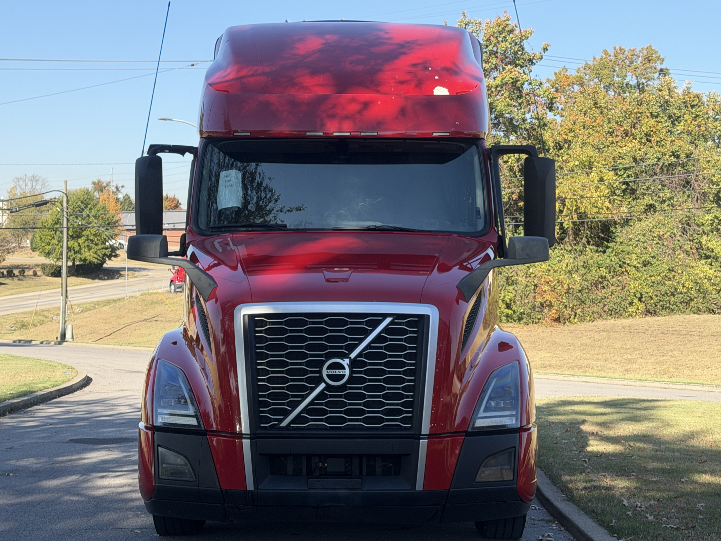 Volvo VNL64T760 cab with red paint and black grille, front view in sunlight.