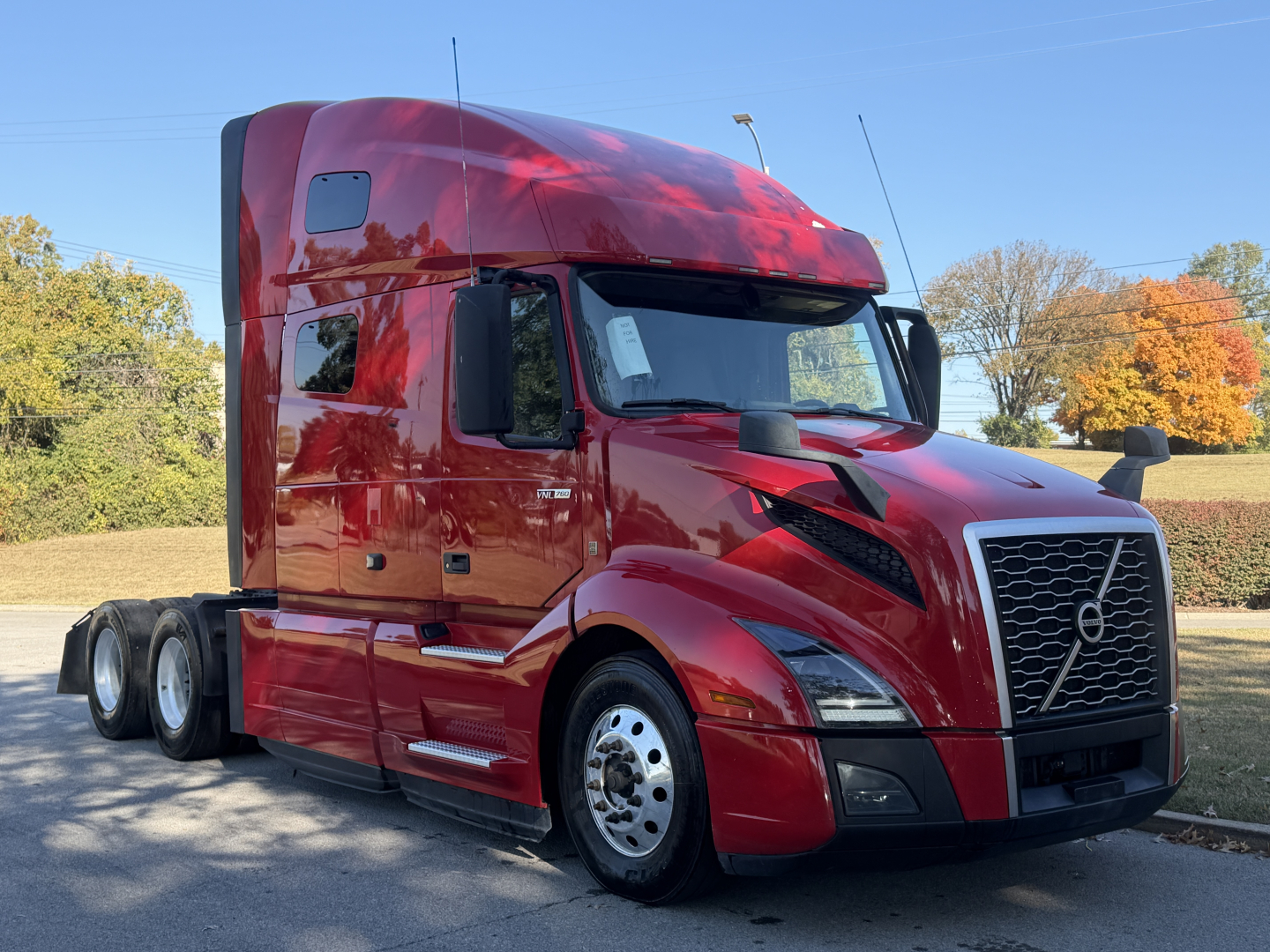 Volvo VNL64T760 tractor-trailer in red, side view showing cab and front grille with Volvo emblem, daytime outdoor setting.
