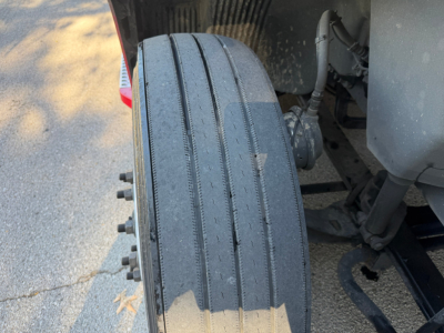 Volvo VNL64T760 truck rear showing a single wide front tire with tread wear, axle components and suspension visible.
