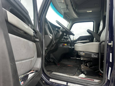 Kenworth T680 truck cab interior with steering wheel, dashboard, and gray driver seat; entry door open, dashboard console visible.