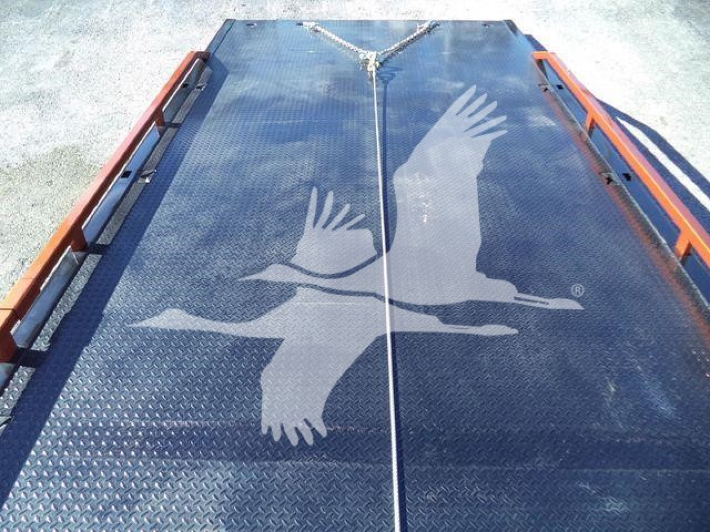 Flatbed truck deck with diamond plate surface and orange side rails, featuring a large fedEx-like logo of two birds in flight on the metal surface.