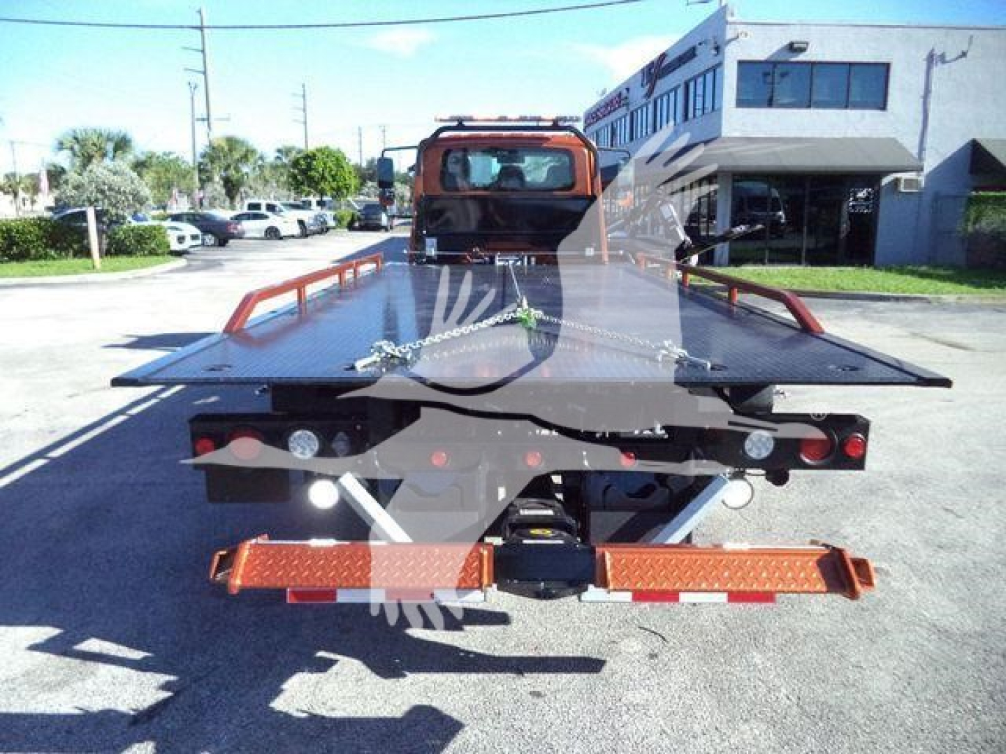 Truck bed of a 2019 International 4300 rollback tow truck viewed from rear showing flatbed, safety lights, and reflective orange rear bumper.