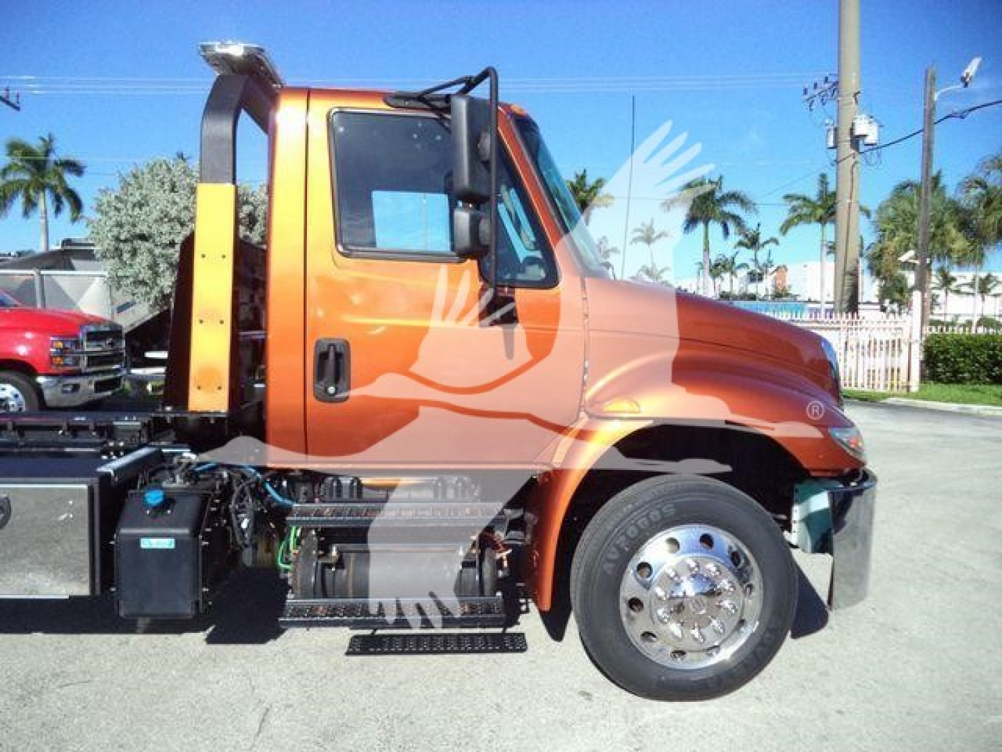 Truck side view showing orange 2019 International 4300 rollback unit with cab, fuel tanks, and chrome wheel on front; stock number T20494FM in background.