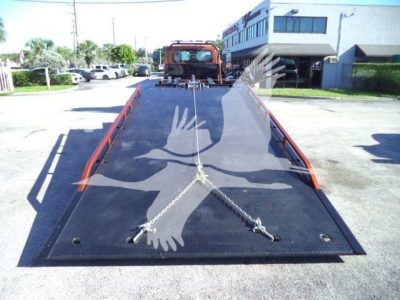 Truck property image showing a flatbed rollback with chain tie-downs and a red cab in the background.