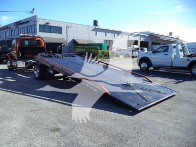 Flatbed tow truck loading plate with a white pickup truck and industrial warehouse in the background.