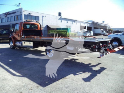 2019 International 4300 rollback truck rear flatbed with equipment and parking lot background.
