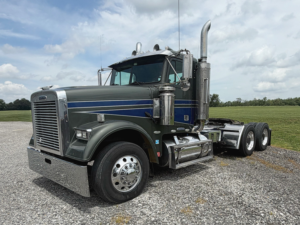 Freightliner FLD12064T Classic heavy-duty truck in profile view showing chrome front bumper, dual exhaust stacks, and large fuel tanks.