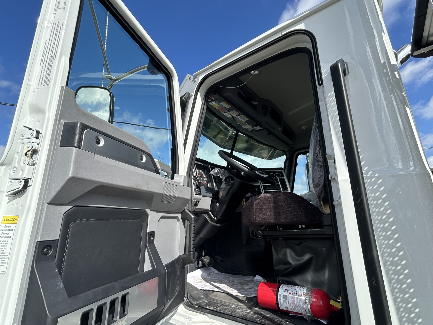 Truck cab interior with open door showing driver seat and dashboard; warning label and control panels visible