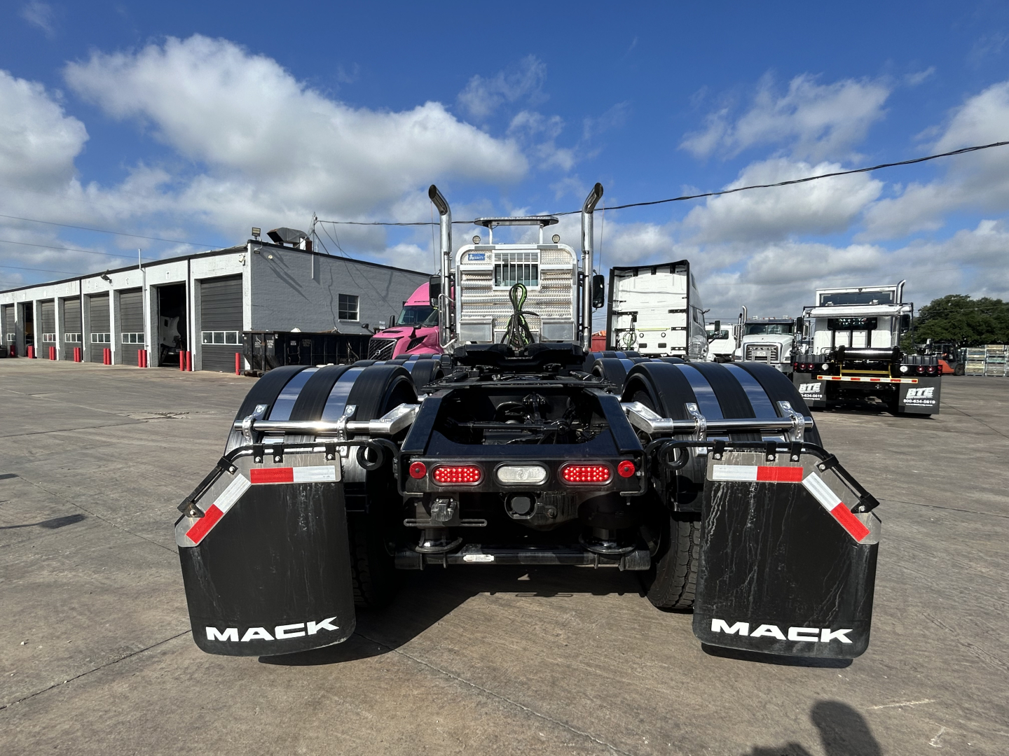 Rear view of a new 2027 Mack GR84FT conventional daycab showing dual rear wheels, black mud flaps with 'MACK' text, and chrome bumper with taillights.