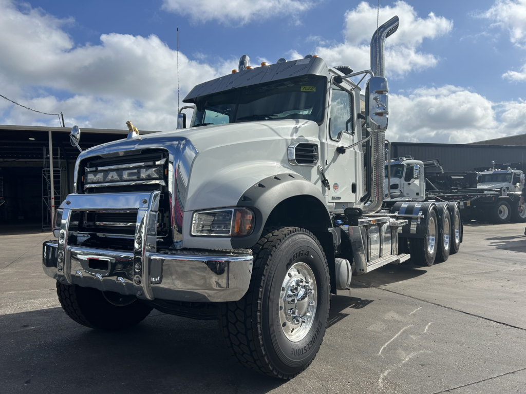 Mack truck in a dealership lot with chrome bumper, large front grille, and dual rear axles. Visible text includes MACK on grille and various chrome accents.