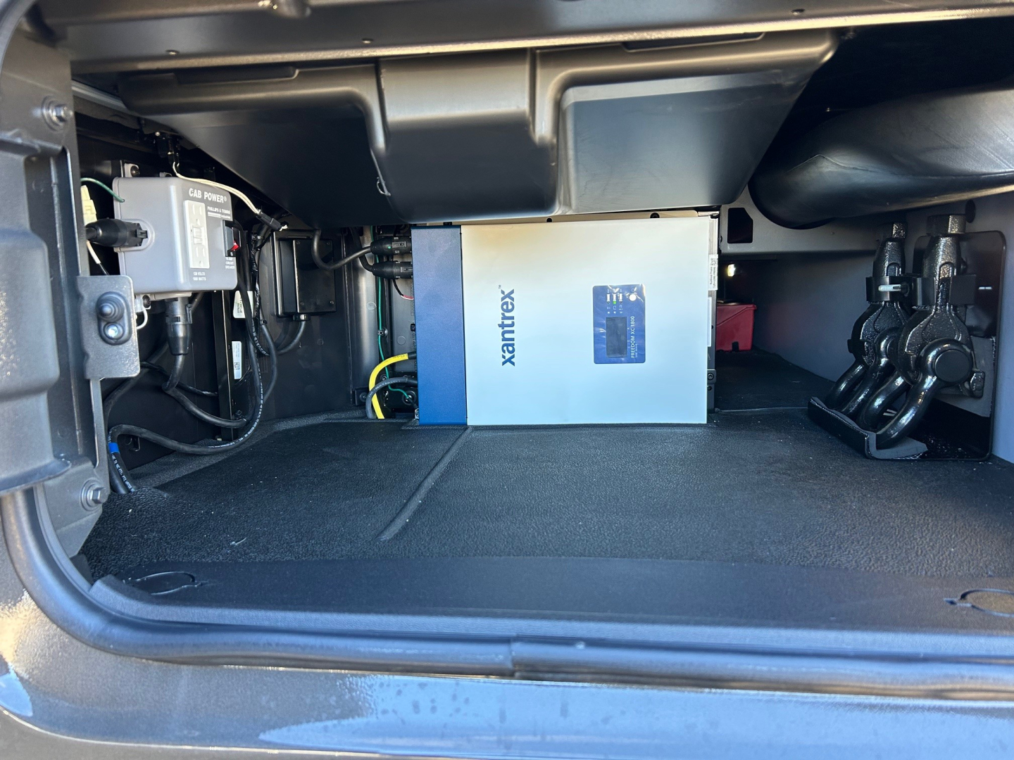 Undertruck storage compartment showing a blue-and-white Xantrex power inverter in a Mack PR64T64M sleeper truck.
