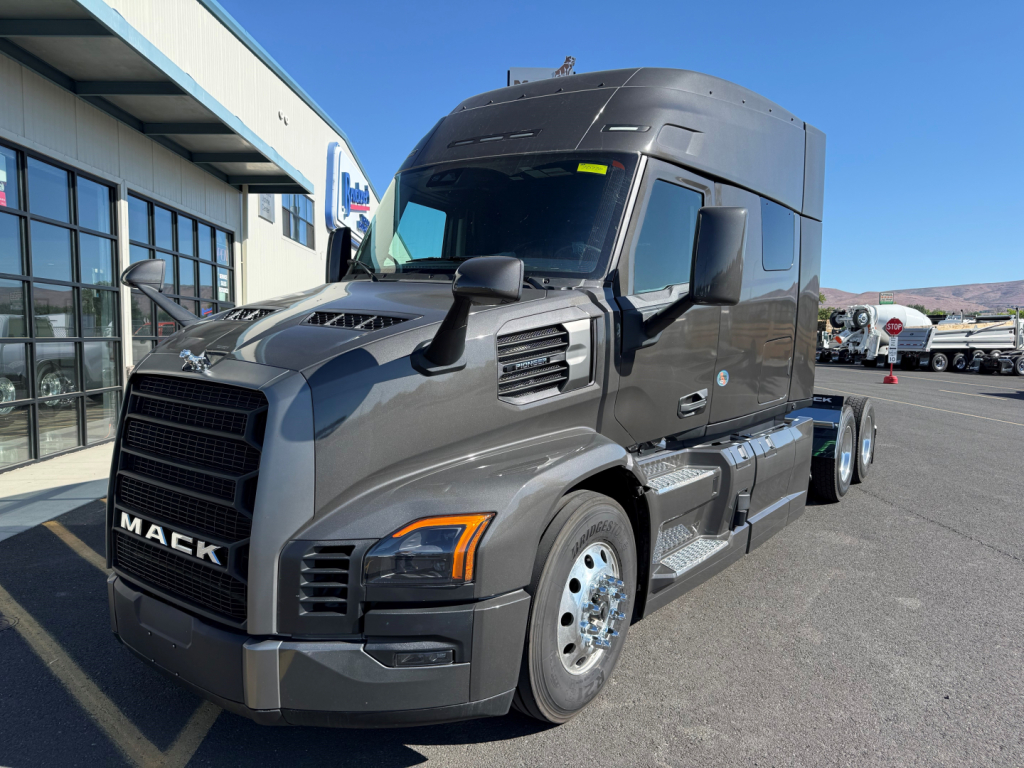 Mack PR64T64M conventional sleeper tractor showing front grille and side view with dark gray paint and large mirrors.