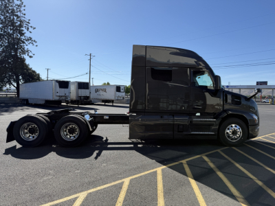 Side view of a black 2026 Mack PR64T64M conventional sleeper truck tractor with a long chassis and three rear axles showing. Visible text includes no explicit labels on the cab in the image.