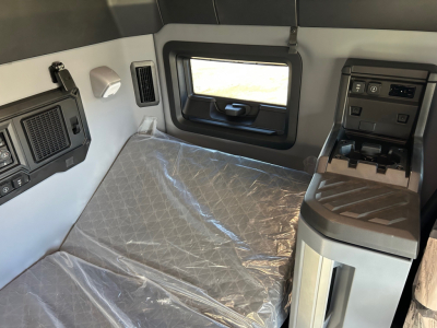 Truck cab interior with sleeper bunk and control panel showing seating area and window.