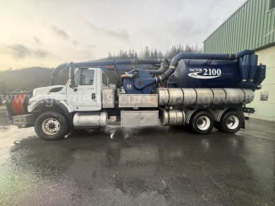 Side view of a 2013 International WorkStar 7500 vacuum truck showing vacuum tank and hoses, with chrome tandem rear axles and white cab.