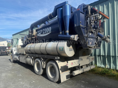 Truck-mounted vacuum tanker unit on a semi-truck chassis showing a large blue vacuum tank and rear equipment with hoses and pumps.
