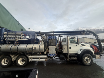 International WorkStar vacuum truck side view showing large black hose reel and tanks; visible text includes '2100' on a blue component near the middle and various pipes and valves.