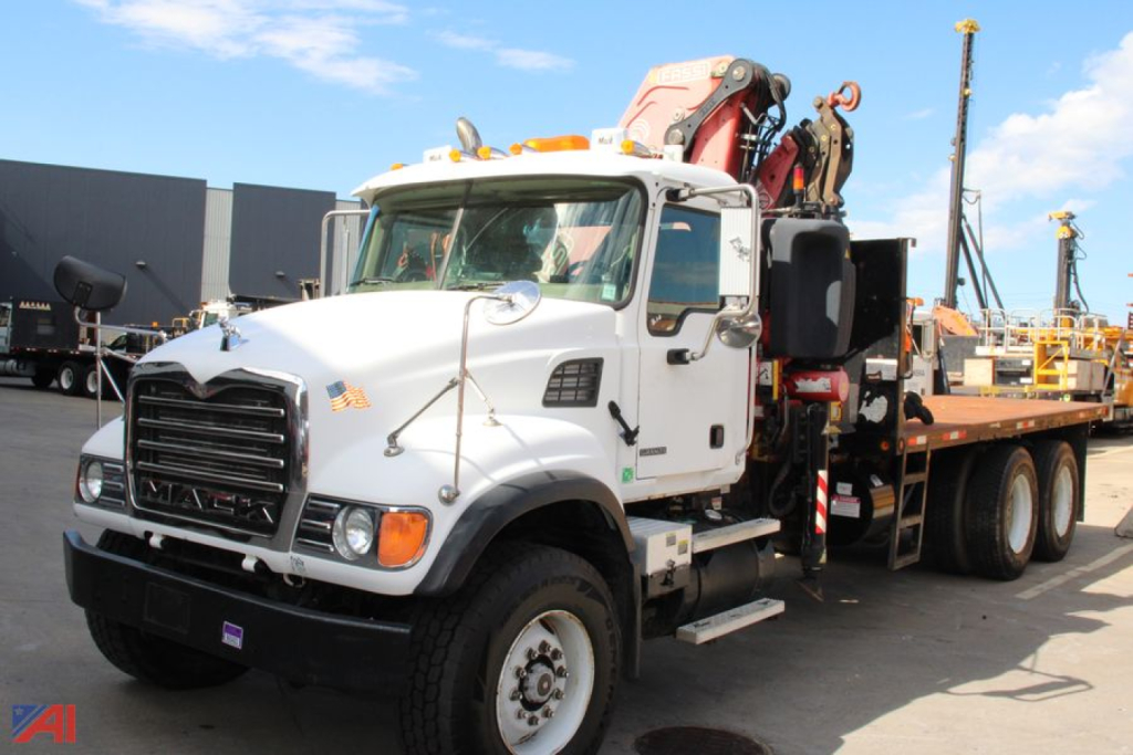 Mack CV713 truck with knuckle boom crane mounted on a flatbed, white cab, front view showing crane apparatus and supporting outriggers.