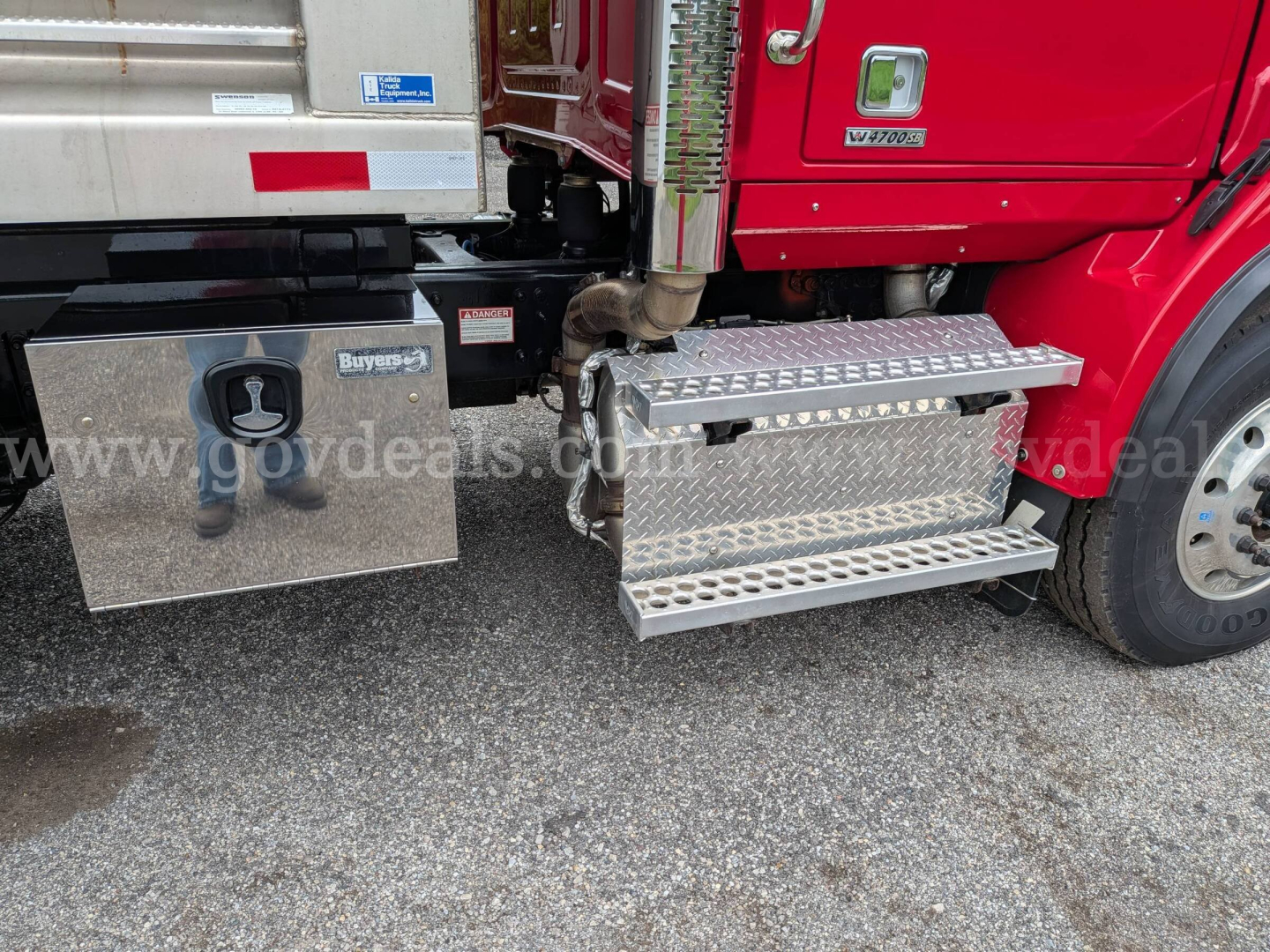 Truck side view showing aluminum toolbox and diamond plate steps attached to a red Western Star 4700 cab with plow equipment in view.