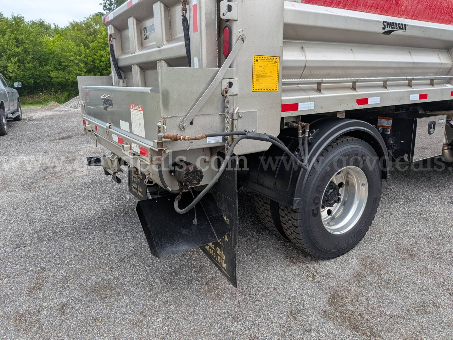 Rear-right view of a used 2015 Western Star 4700 dump truck with plow. Visible components include rear mud flap, dump bed side, hydraulic hoses, and wheel with tire. Includes stock tag area and reflective stripes.