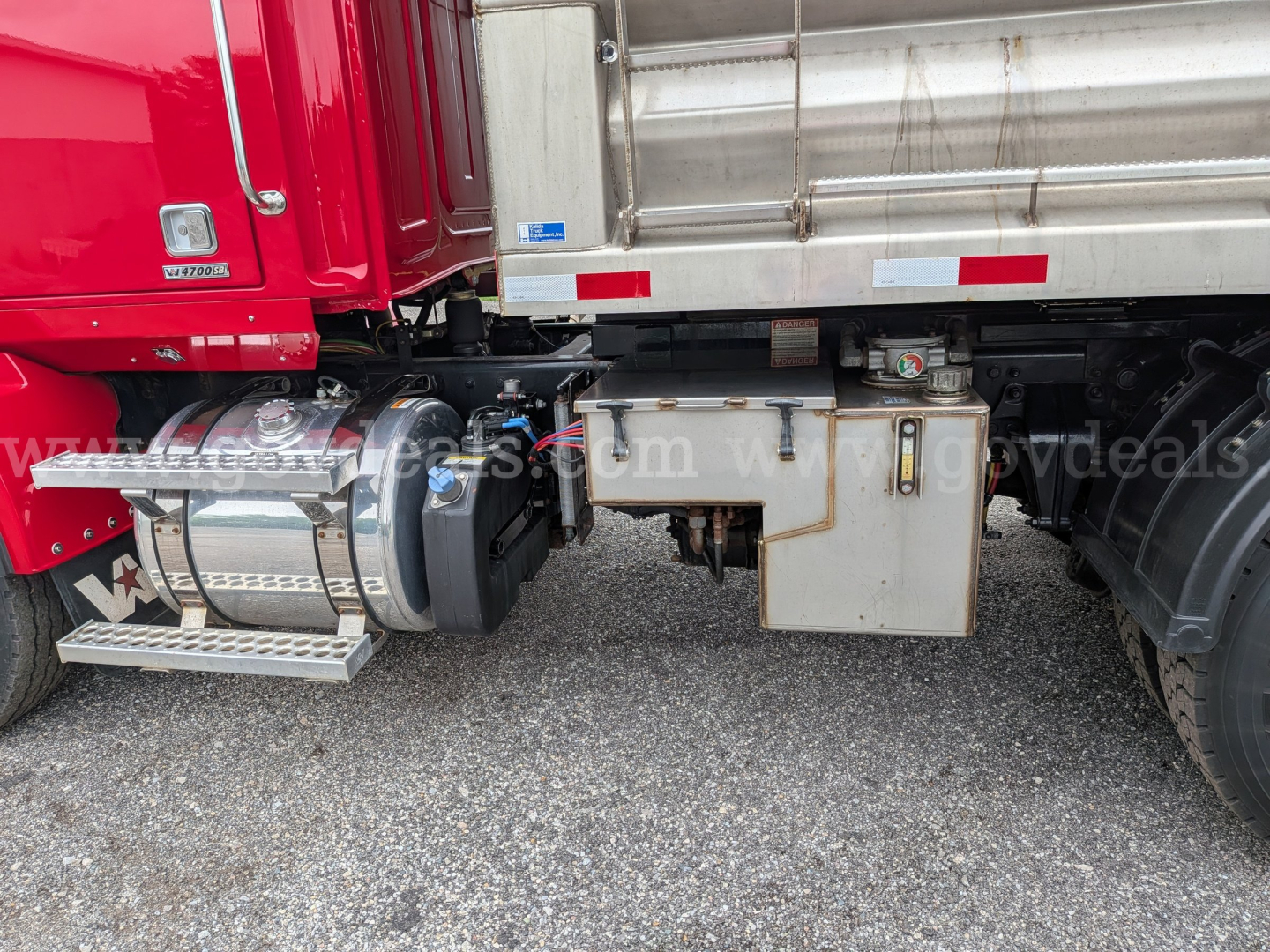 Side view of a red Western Star 4700 truck with a silver dump bed. Visible text includes partial VIN plate and stock number area, plus miscellaneous labels on the chassis and fuel tanks.