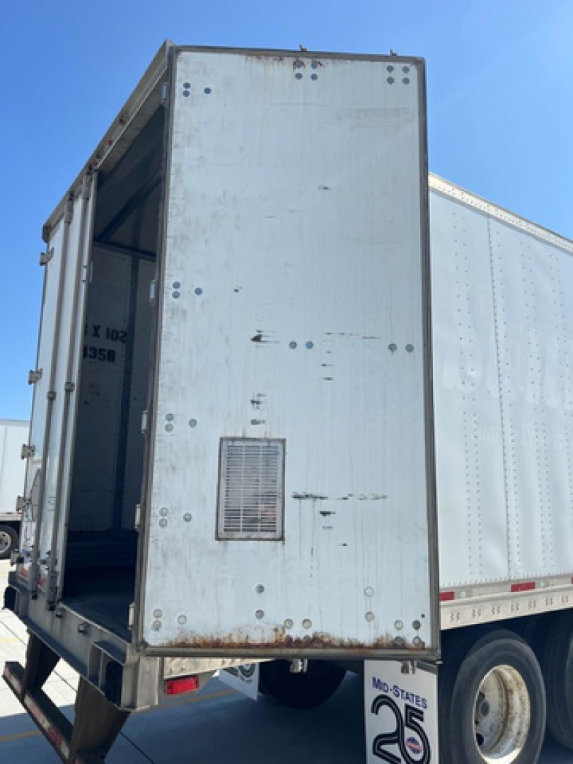 Rear cargo area of a box trailer with open rear door, showing riveted metal exterior, small vent, and lower bumper area.