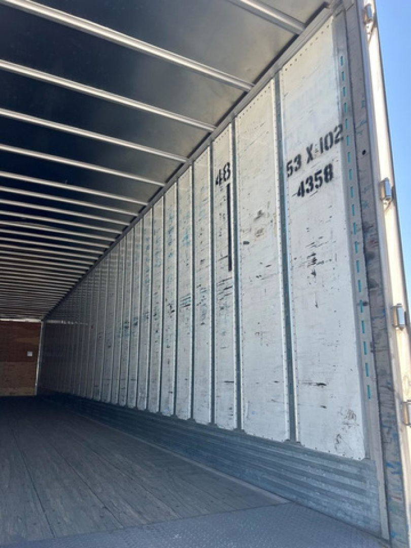 Trailer interior showing metal side walls with vertical ribbing and numbers 48, 53 X 102, 4358 along the door, empty cargo space.