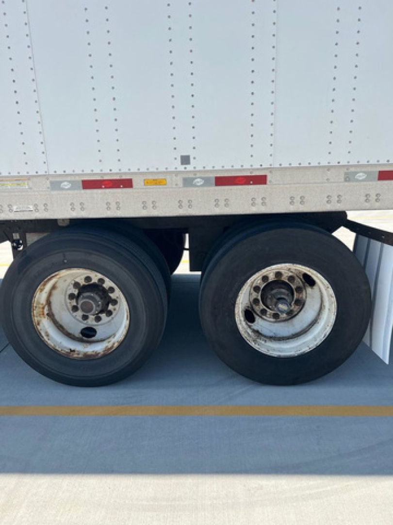 Dual rear trailer wheels and a portion of a box trailer side with riveted metal and reflective tape.