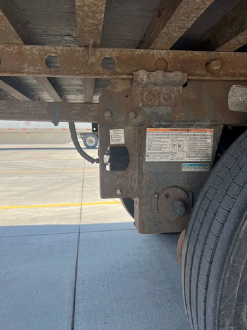 Trailer hitch area with identification labels on the frame and a portion of the wheel. Visible text includes a rectangular label with small print and a VIN-like plate near the left side.