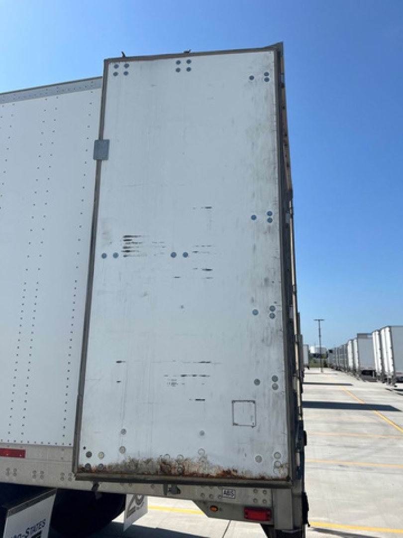 Trailer rear door of a utility van/trailer showing white metal surface with rivets and rust at the bottom edge.